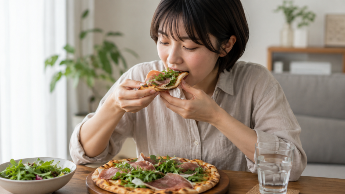 生ハムとルッコラのピザを手で持って食べる日本人女性